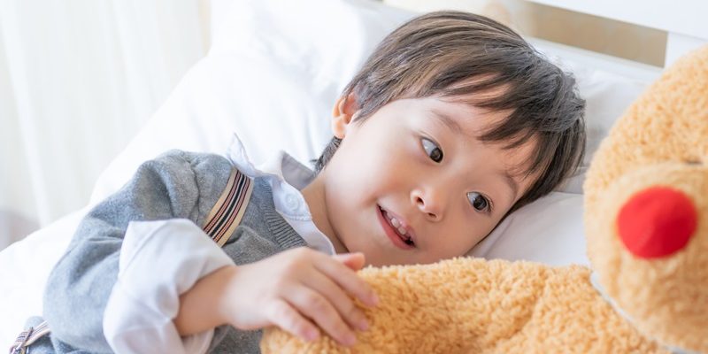 Little boy playing with large teddy bear on bed