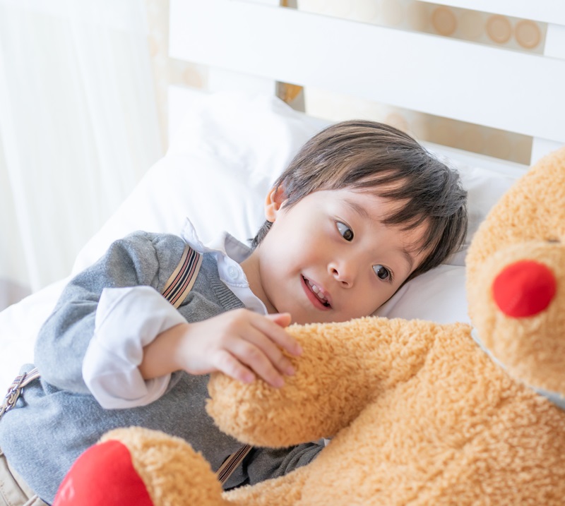 Little boy playing with large teddy bear on bed