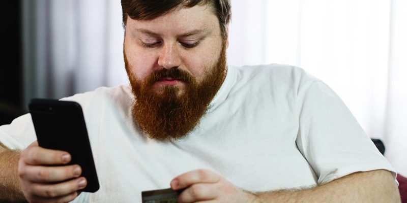 Fat man types the number of a credit card in his phone sitting o